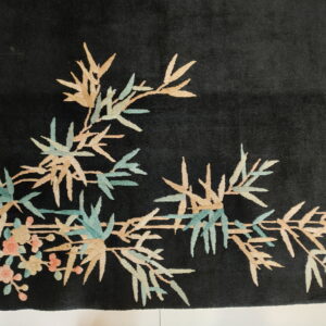 Close-up of a black rug showing light beige and teal bamboo leaves and coral pink blossoms.