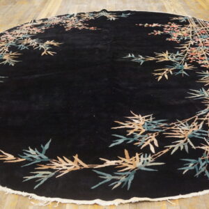 Oval black rug with sprawling bamboo and blossom border in tan, teal, and pink on wood planks.