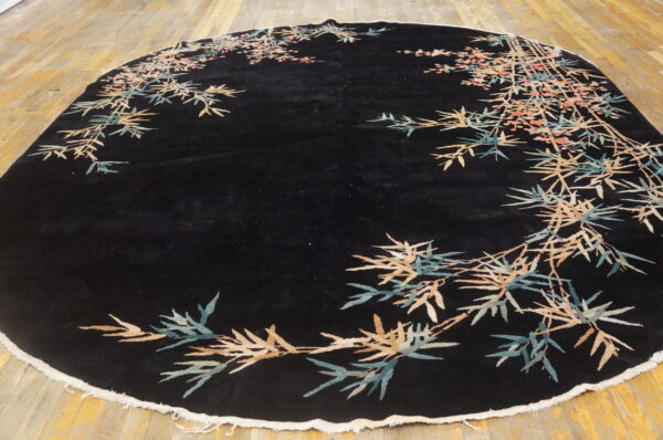 Oval black rug with sprawling bamboo and blossom border in tan, teal, and pink on wood planks.