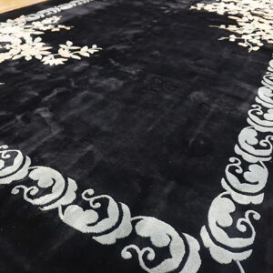 A black rug featuring white floral sprays and a light grey scroll border on wood floor.