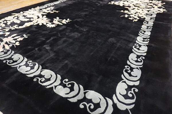 A black rug featuring white floral sprays and a light grey scroll border on wood floor.