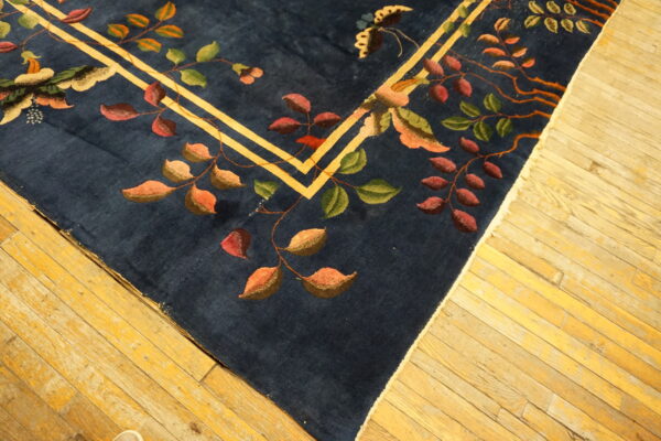 Close-up of a navy rug with multicolored floral vines and a yellow border on distressed wood flooring.