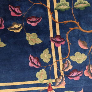 Dark blue rug featuring a botanical pattern of green and pink leaves, orange branches, and intersecting gold stripes.