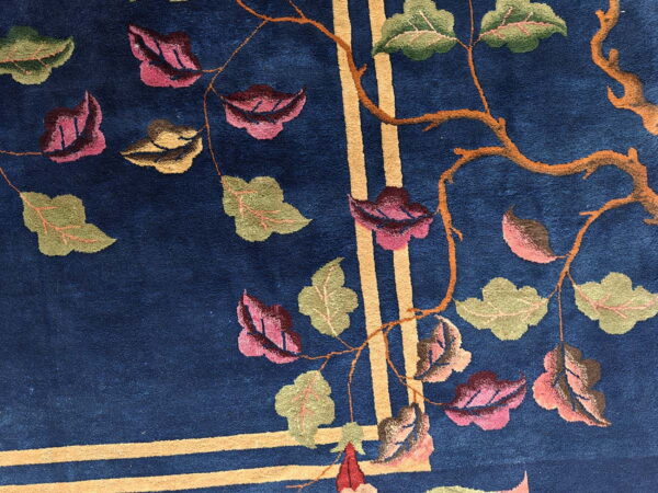 Dark blue rug featuring a botanical pattern of green and pink leaves, orange branches, and intersecting gold stripes.