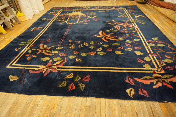 Dark blue plush rug featuring a vibrant floral pattern and gold border on light wood flooring.