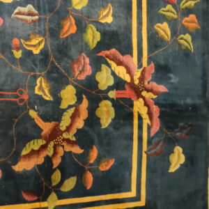 Dark blue rug with a floral pattern of red, green, and gold motifs, framed by bold yellow-gold double stripes.