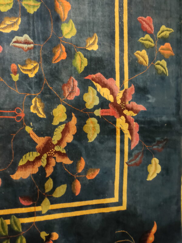 Dark blue rug with a floral pattern of red, green, and gold motifs, framed by bold yellow-gold double stripes.