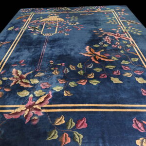 A plush blue rug with a stylized floral and bird pattern framed by an ochre double-line border.