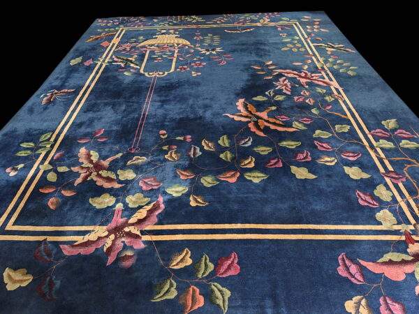 A plush blue rug with a stylized floral and bird pattern framed by an ochre double-line border.