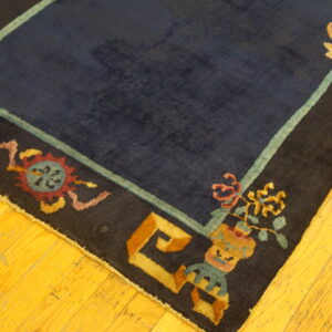 Dark blue rug with a multicolored stylized border rests on polished yellow hardwood floorboards.