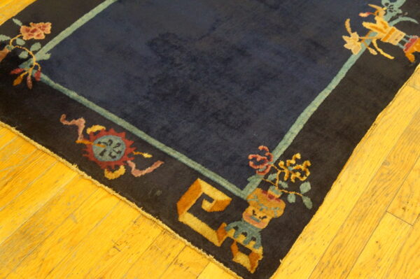 Dark blue rug with a multicolored stylized border rests on polished yellow hardwood floorboards.