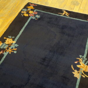 Navy high-pile rug featuring black borders and colorful floral corner motifs on yellow hardwood flooring.