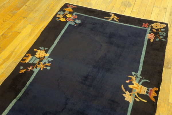 Navy high-pile rug featuring black borders and colorful floral corner motifs on yellow hardwood flooring.