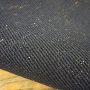 Detail of a dark blue corded rug surface featuring numerous light natural fiber flecks.