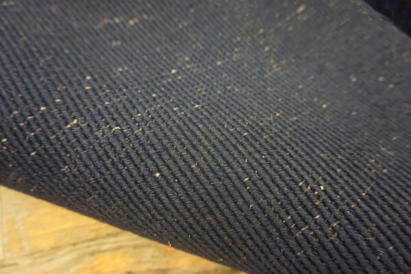 Detail of a dark blue corded rug surface featuring numerous light natural fiber flecks.
