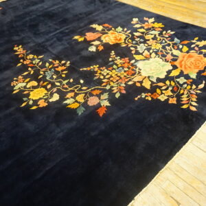 A velvety navy rug displaying large bright floral designs rests on distressed light wood floorboards.