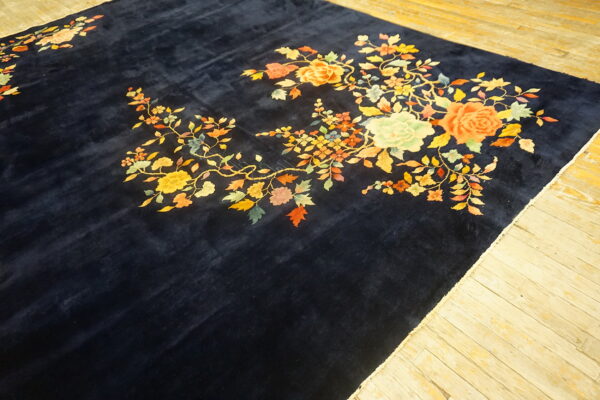 A velvety navy rug displaying large bright floral designs rests on distressed light wood floorboards.