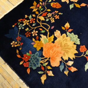 Dark blue high-pile rug featuring a vibrant multicolored floral and vine pattern on light wood flooring.