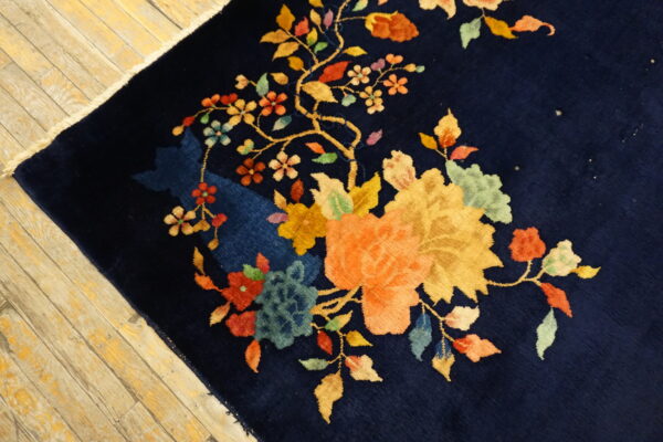 Dark blue high-pile rug featuring a vibrant multicolored floral and vine pattern on light wood flooring.