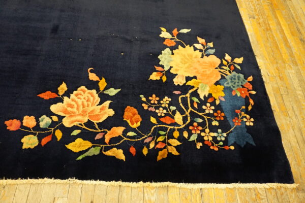 Navy rug featuring bright yellow and peach flowers and green leaves on aged plank flooring.