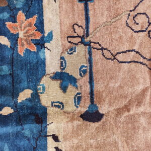Textured close-up of a rug with deep blue, orange floral, and dark scrollwork on a dusty tan field.