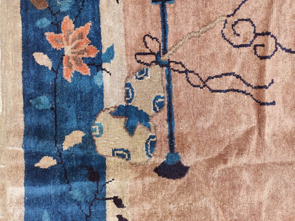 Textured close-up of a rug with deep blue, orange floral, and dark scrollwork on a dusty tan field.