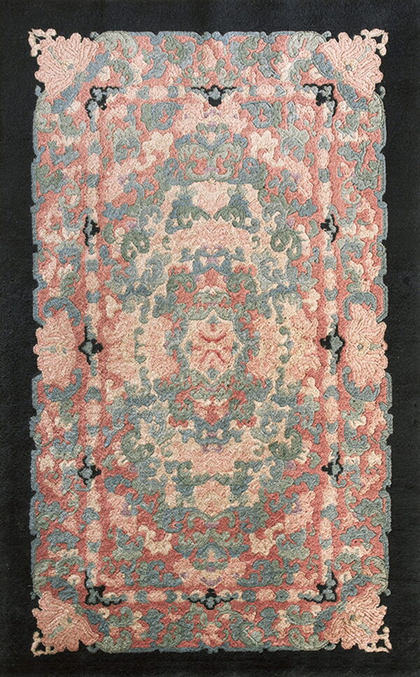 Pink, sage, and blue traditional rug with a carved floral pattern and scalloped edges on a dark backdrop.
