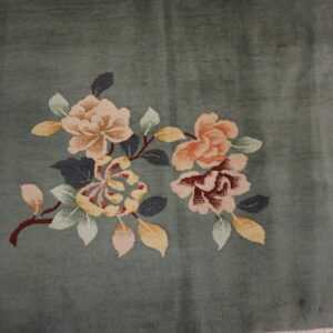 Muted green rug with clustered pink, gold, and red floral designs beside rustic wood planks.