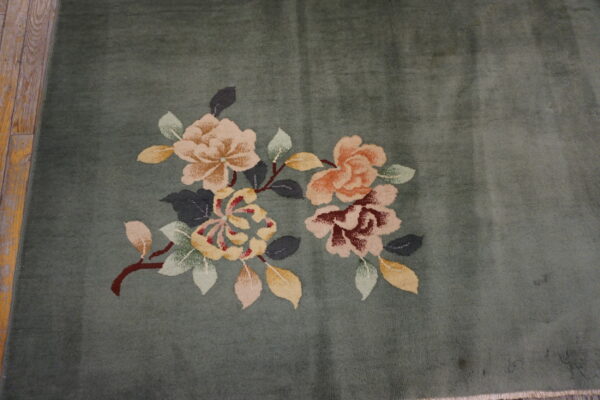 Muted green rug with clustered pink, gold, and red floral designs beside rustic wood planks.