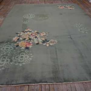 Plush, muted green rug featuring asymmetric pale pink and yellow floral sprays on worn wood planks.