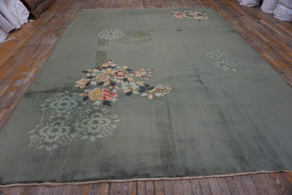 Plush, muted green rug featuring asymmetric pale pink and yellow floral sprays on worn wood planks.