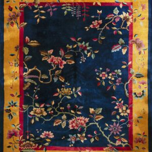 A deep blue rug with a gold border and intricate multi-colored floral and vine patterns.