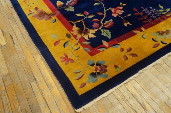 Navy blue rug with a wide golden yellow floral border sits on distressed light wood floors.