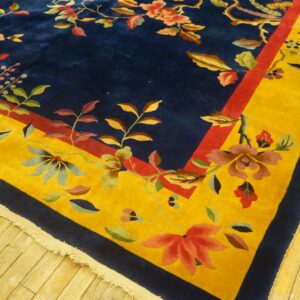 Navy blue rug with a dense floral pattern and a wide yellow and red border on wood planks.