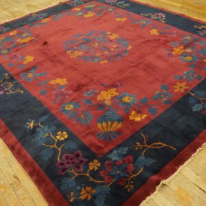 A large red floral rug with a deep navy border and lustrous low pile lies on light hardwood.