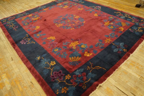 A large red floral rug with a deep navy border and lustrous low pile lies on light hardwood.