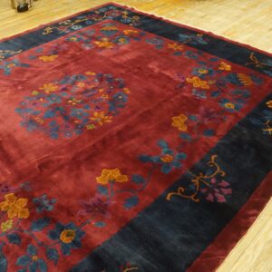A burgundy rug featuring gold, blue, and purple floral motifs with a wide navy border rests on hardwood flooring.