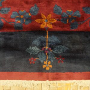 Plush navy and red floral rug border with yellow accents and white fringe on wood flooring.