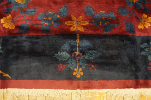 Plush navy and red floral rug border with yellow accents and white fringe on wood flooring.