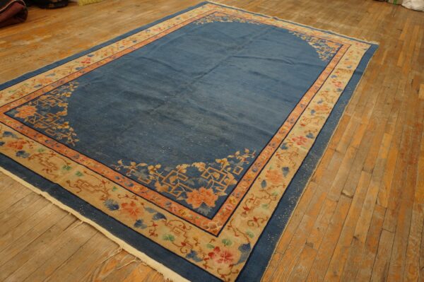 Blue rug with a large tan floral border and coral accents laid upon rustic wooden floors.