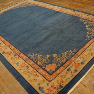 Large blue rug with wide beige and coral borders, featuring floral patterns on wood floors.
