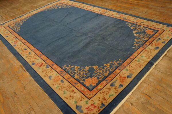 Large blue rug with wide beige and coral borders, featuring floral patterns on wood floors.