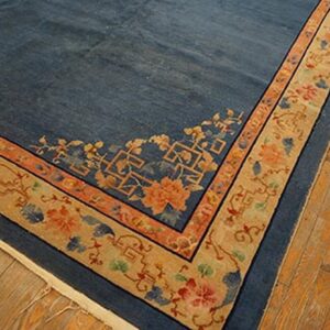 Dark blue rug with a wide tan border patterned with orange and blue floral motifs on wood flooring.