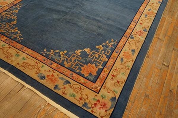 Dark blue rug with a wide tan border patterned with orange and blue floral motifs on wood flooring.