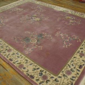 Low pile rug in dusty rose with floral patterns and a wide pale border on worn wood floors.