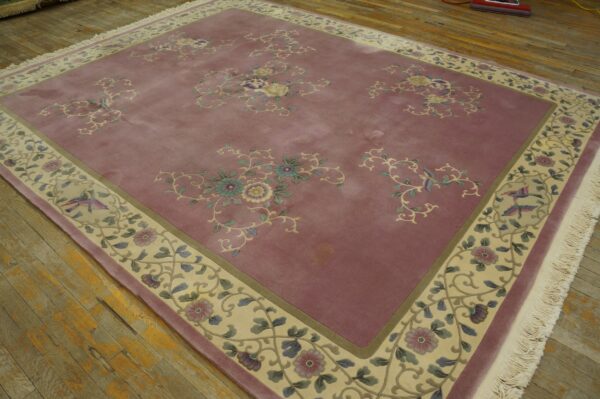 Low pile rug in dusty rose with floral patterns and a wide pale border on worn wood floors.