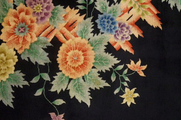 Close-up of a black rug with large, colorful floral and leafy motifs in orange, purple, blue, and green.