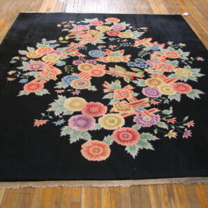 Plush black rug with a dense cluster of multicolored floral patterns lying on wooden planks.
