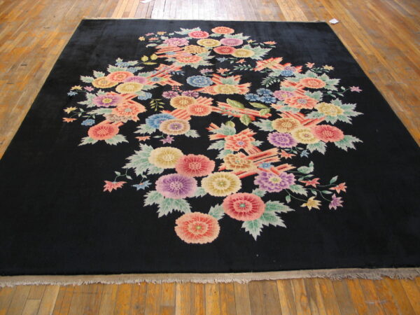 Plush black rug with a dense cluster of multicolored floral patterns lying on wooden planks.