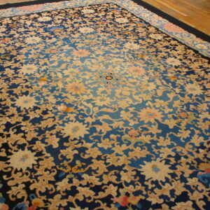 Ornate floral rug with navy, cerulean, and beige colors resting on light brown hardwood flooring.